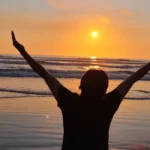 Silhueta de pessoa agradecendo a Deus no amanhecer dourado na praia - bom dia abençoado
