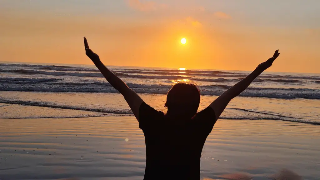 Silhueta de pessoa agradecendo a Deus no amanhecer dourado na praia - bom dia abençoado
