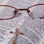 Óculos sobre Bíblia aberta com cruz de metal, representando estudo do Salmo 139 e reflexão espiritual